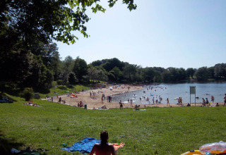 Lakeside beach with swimmers and sunbathers at Campsite Seasonova Lac de Bournazel in Nouvelle-Aquitaine, France.
