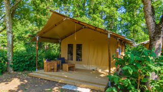 Safari tent Slow lodge met 2 slaapkamers, houten zitje op terras, omgeven door groene natuur.