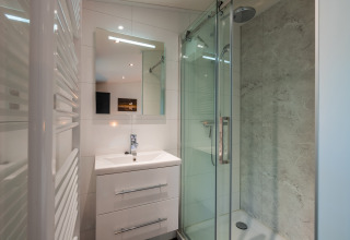 Baño moderno en Zandborg Lodge, De Wiltzangh, Países Bajos, con ducha de cristal y lavabo.