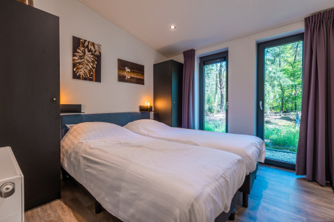 Dormitorio moderno con dos camas individuales, ventanas grandes y vista al bosque en Zandborg Lodge, De Wiltzangh.
