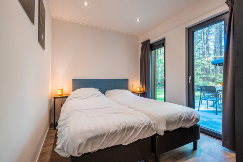 Bedroom at Zandborg Lodge, Holiday park De Wiltzangh, with twin beds and view of private terrace and woods.