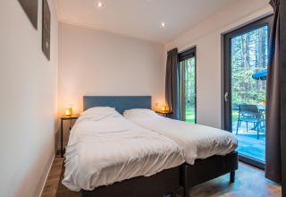 Slaapkamer in Zandborg Lodge, Holiday park De Wiltzangh, met twee bedden en zicht op privéterras en bos.