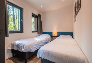 Lyst værelse med to enkeltsenge, store vinduer og minimalistisk indretning i Zandborg Lodge, Holiday park De Wiltzangh.