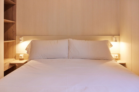 Dormitorio del Bungalow «Confort Poniente» en TAIGA Conil, España, con cama cómoda y luz cálida.