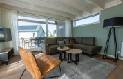 Wohnzimmer in Duinlodge 6 im EuroParcs Cadzand-Bad, Niederlande, mit Sofa, Sessel und großen Fenstern.