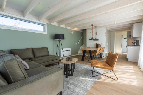 Moderne stue i Duinlodge 6 ved EuroParcs Cadzand-Bad, Holland, med grøn sofa og spisebord.