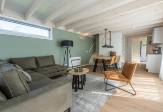 Moderne stue i Duinlodge 6 ved EuroParcs Cadzand-Bad, Holland, med grøn sofa og spisebord.