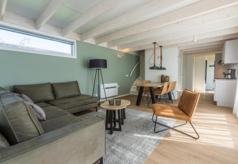 Moderne stue i Duinlodge 6 ved EuroParcs Cadzand-Bad, Holland, med grøn sofa og spisebord.