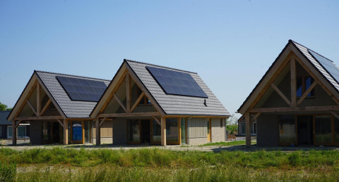 Drie moderne lodges met zonnepanelen op het dak bij EuroParcs Cadzand-Bad in Nederland onder blauwe lucht.