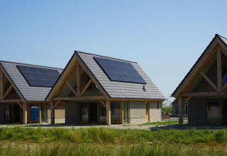 Drie moderne lodges met zonnepanelen op het dak bij EuroParcs Cadzand-Bad in Nederland onder blauwe lucht.