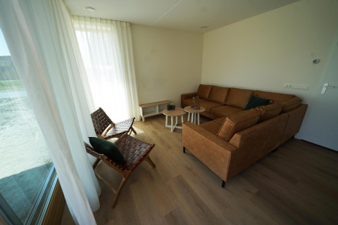 Woonkamer van Duinvilla 10 bij EuroParcs Cadzand-Bad, Nederland, met bruine bank en lichte gordijnen.