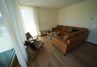 Woonkamer van Duinvilla 10 bij EuroParcs Cadzand-Bad, Nederland, met bruine bank en lichte gordijnen.