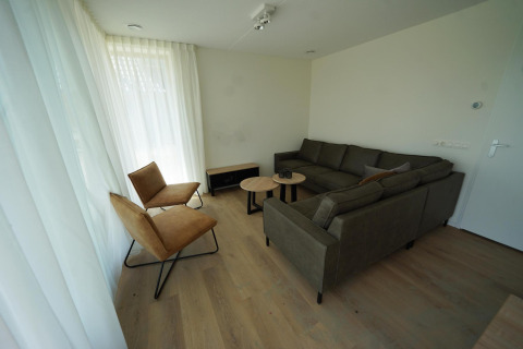 Woonkamer in Duinvilla 10 bij EuroParcs Cadzand-Bad met bank, twee stoelen, tafeltjes en lichte gordijnen.