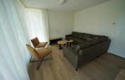 Wohnzimmer in Duinvilla 10 bei EuroParcs Cadzand-Bad mit Sofa, zwei Stühlen, Tischen und Vorhängen.