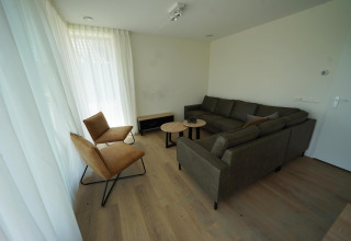 Woonkamer in Duinvilla 10 bij EuroParcs Cadzand-Bad met bank, twee stoelen, tafeltjes en lichte gordijnen.