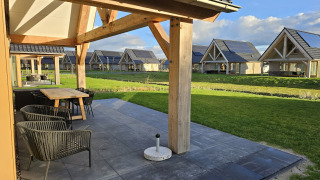 Zonnig uitzicht op terrassen en moderne houten lodges bij Duinvilla 6, omringd door groene gazons.