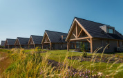 Mehrere Duinvilla 6 Lodges im EuroParcs Cadzand-Bad, Niederlande, mit grünen Gärten und blauem Himmel darüber.