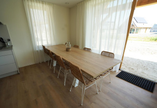 Eethoek in lodge «Duinvilla» 10 bij EuroParcs Cadzand-Bad, Nederland, met grote houten tafel en stoelen.