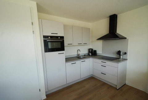 Moderne keuken in een lodge bij EuroParcs Cadzand-Bad met witte kasten, zwarte handgrepen en apparatuur.
