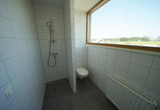 Moderne badkamer met douche, hangend toilet en groot raam in Duinvilla 10 bij EuroParcs Cadzand-Bad.