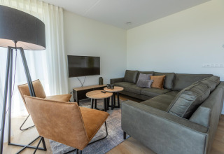 Soggiorno moderno nella Duinvilla 8 a EuroParcs Cadzand-Bad, Paesi Bassi, con divano grigio e poltrone in pelle.