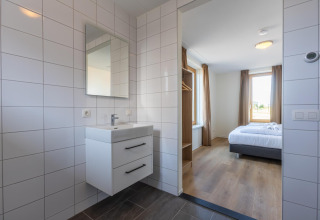 Bagno moderno con piastrelle bianche e vista sulla camera da letto a Duinvilla 8, EuroParcs Cadzand-Bad, Paesi Bassi.