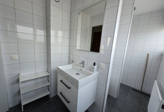 Bagno moderno in una lodge con piastrelle bianche, lavabo doppio, specchio e scaffale semplice.