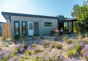 Modern lodge met terras waar mensen genieten in de zon, omringd door bloemen en natuur.