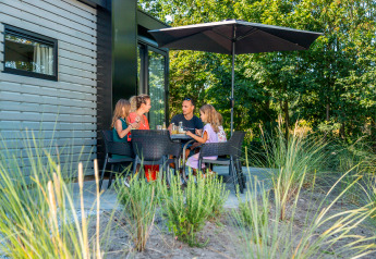 Famiglia che gusta un pasto sulla terrazza di un lodge sotto un ombrellone, immersa nel verde.