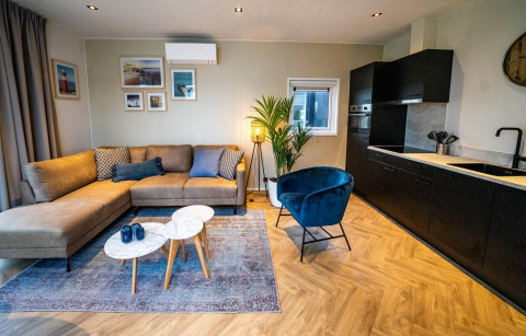 Moderne woonkamer in de Pavilion-lodge bij EuroParcs Texel, met bank, blauwe stoel, keuken en decoratie.