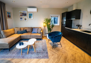 Moderne woonkamer in de Pavilion-lodge bij EuroParcs Texel, met bank, blauwe stoel, keuken en decoratie.