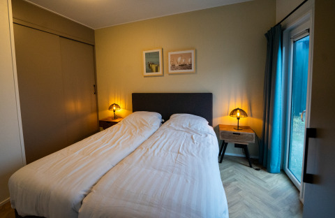 Gezellige slaapkamer in een lodge met twee eenpersoonsbedden, nachtkastjes, lampen en terrasdeur.