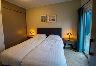 Gezellige slaapkamer in een lodge met twee eenpersoonsbedden, nachtkastjes, lampen en terrasdeur.