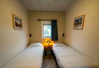 Stanza accogliente di un lodge con due letti singoli, lampada da comodino e finestra con tenda.