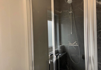 Doccia moderna con porte in vetro e piastrelle scure nel bagno di un lodge Pavilion a EuroParcs Texel.