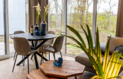 Interior de lodge moderno con mesa redonda, sillas, plantas y ventanas grandes en EuroParcs Texel.