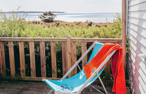 Liegestuhl mit orangem Handtuch auf einer Terrasse mit Meerblick im Flower Camping La Pointe du Talud, Bretagne.
