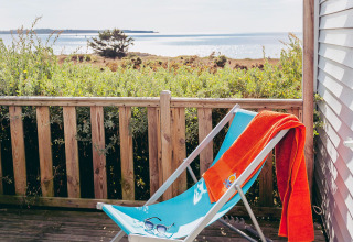 Liegestuhl mit orangem Handtuch auf einer Terrasse mit Meerblick im Flower Camping La Pointe du Talud, Bretagne.