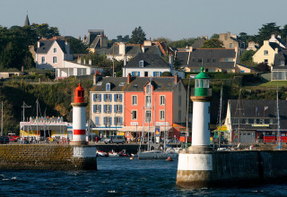 Kuststad nabij Ploemeur in Bretagne, Frankrijk, met gekleurde huizen, haven en twee vuurtorens aan het water.
