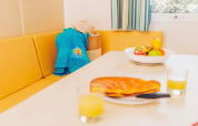 Dining area in Comfort BAHIA mobile home with yellow bench, fruit bowl, and juice at Flower Camping La Pointe du Talud.