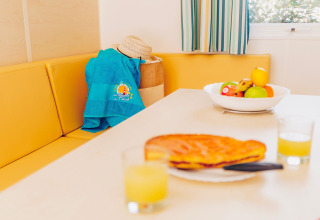 Zona pranzo nella casa mobile Comfort BAHIA con panca gialla, fruttiera e succo, Flower Camping La Pointe du Talud.