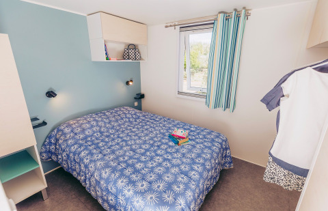 Bedroom in Mobile home Comfort BAHIA at Flower Camping La Pointe du Talud, France, with blue bedspread.