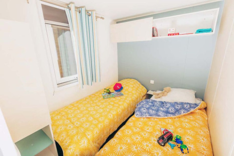 Camas individuales con colchas amarillas en Mobile home Comfort BAHIA en Flower Camping La Pointe du Talud, Francia.