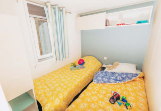 Camas individuales con colchas amarillas en Mobile home Comfort BAHIA en Flower Camping La Pointe du Talud, Francia.