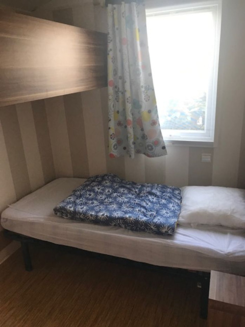 Room in a mobile home with a single bed, colorful curtain at the window, and simple modern decor.