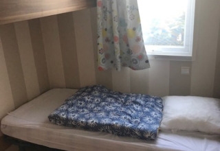 Room in a mobile home with a single bed, colorful curtain at the window, and simple modern decor.