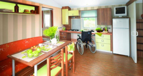 Accessible mobile home kitchen with wheelchair, dining table, and modern decor at Flower Camping La Pointe du Talud.
