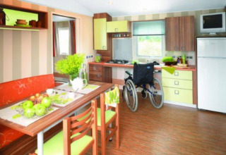 Accessible mobile home kitchen with wheelchair, dining table, and modern decor at Flower Camping La Pointe du Talud.