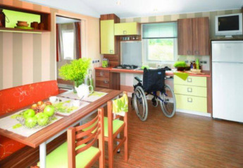 Cocina de casa móvil accesible con silla de ruedas, mesa de comedor y decoración moderna en La Pointe du Talud.