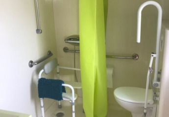 Accessible bathroom in a mobile home with support bars, shower chair, and bright green shower curtain.